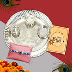Traditional Raksha Bandhan gift set with ornate Rakhi, silver-plated pooja thali, roli-chawal in handcrafted bowls, and a festive greeting card radiating cultural elegance.